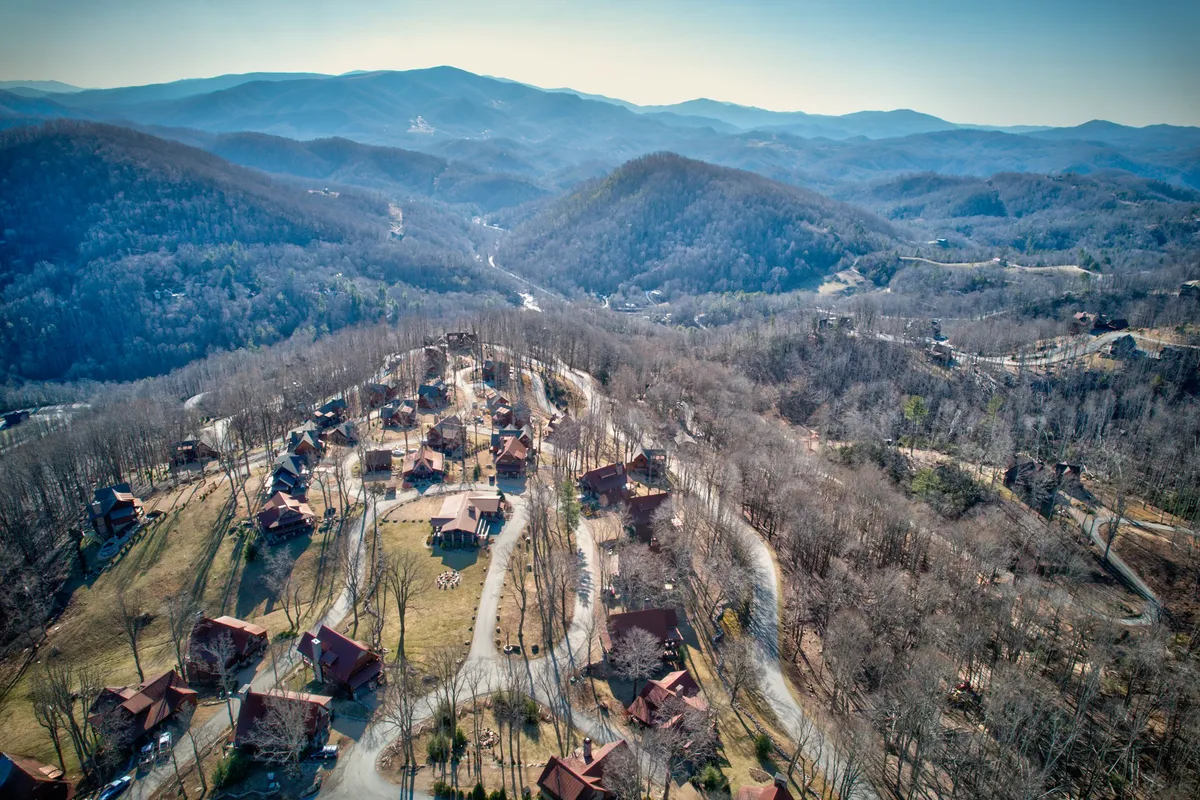 The image shows a serene mountainous landscape dotted with a cluster of cabins and winding roads. The expansive view captures the spirit of exploration and the diverse adventure options available, from hiking and wildlife watching to stargazing and family gatherings.