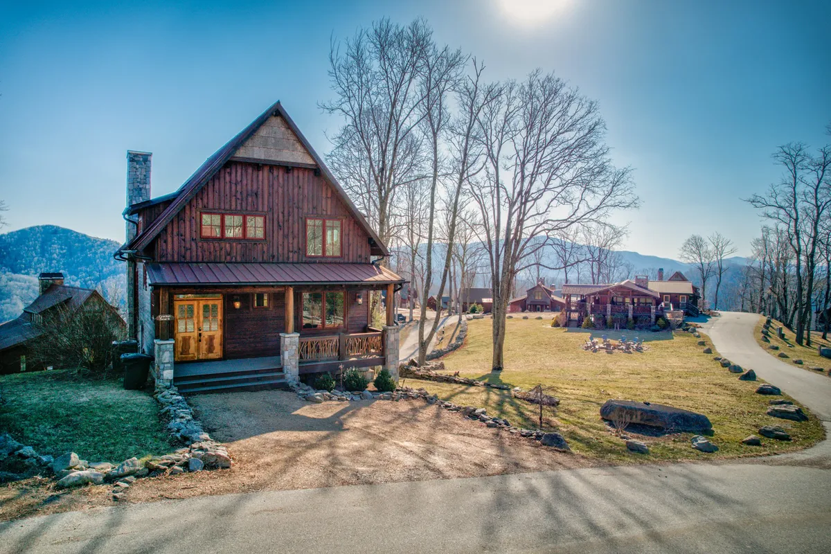 A welcoming view of the main house surrounded by trees, with a scenic mountain backdrop and a pathway leading into the property. The porch and grounds suggest areas for family relaxation, barbecues, and outdoor gatherings, reinforcing the sense of easy access to amenities and nature trails.