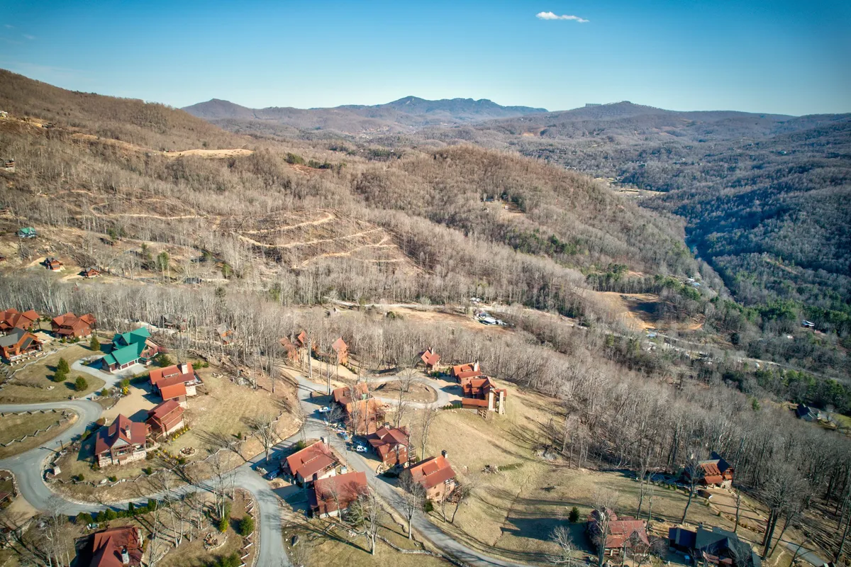 A panoramic exterior view showing a scenic mountain range, a cluster of cozy cabins, and a winding road leading into the natural landscape. The setting is open and inviting, ideal for outdoor activities like hiking, nature walks, and family picnics.