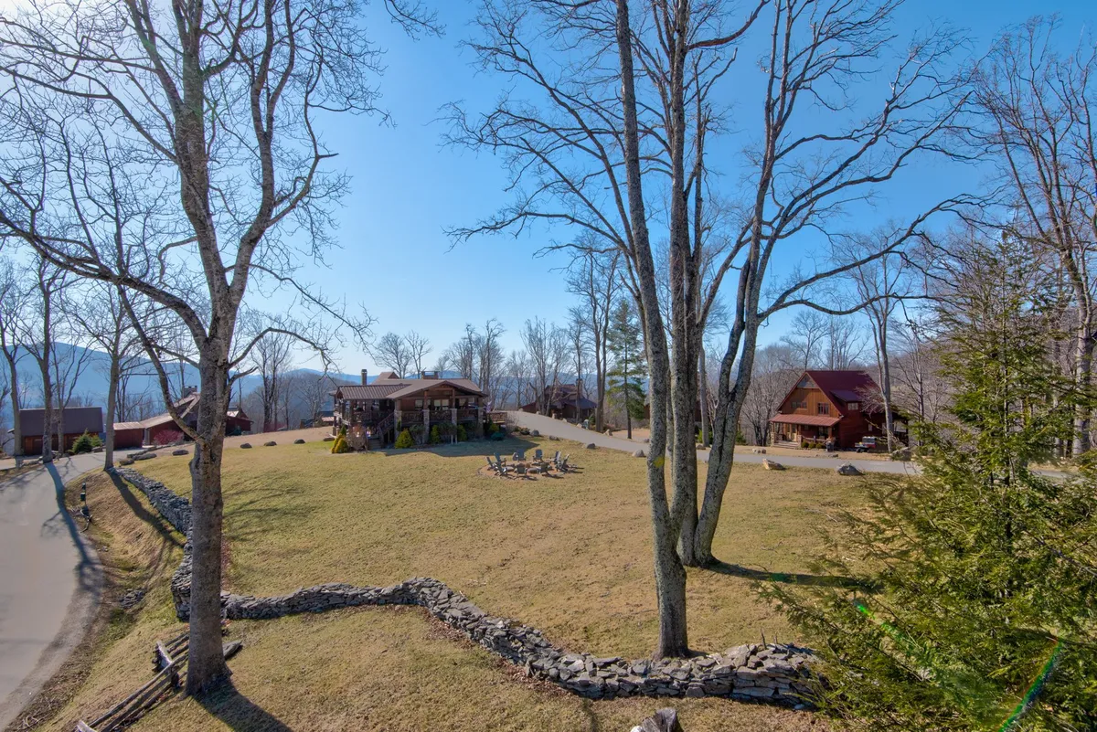 This image features a large main house surrounded by trees, a cozy fire pit area, and a secondary cabin. The outdoor space is inviting and designed for gatherings, highlighting both relaxation and the opportunity for communal fun.