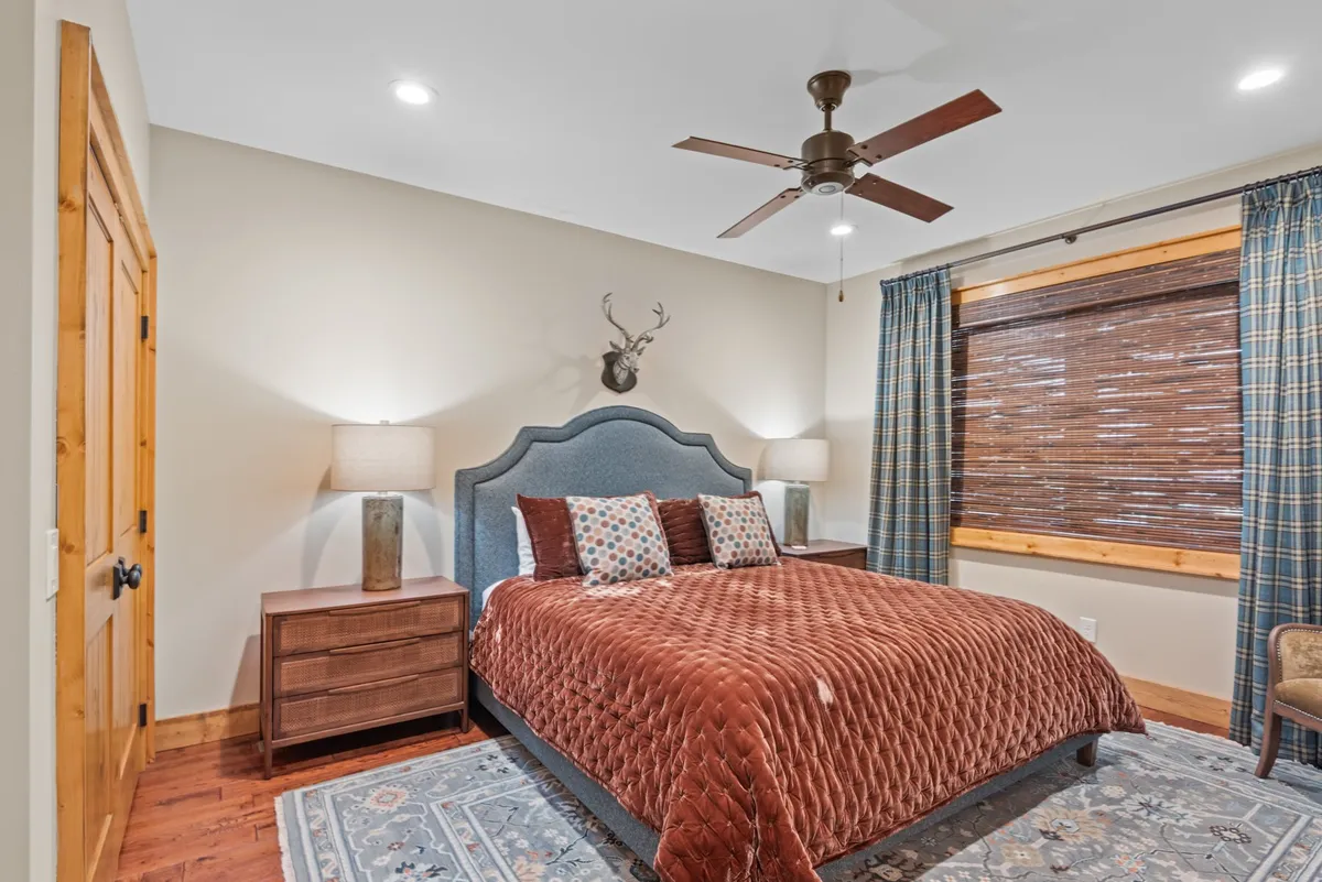 A serene king bedroom with a stylish bed, decorative wall mount, matching nightstands, and soft curtains. The room feels inviting and peaceful, complemented by subtle mountain-inspired decor touches.