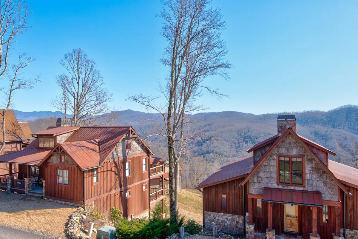 A scenic panorama of rustic wooden houses against a backdrop of rolling mountains and a clear blue sky. The tranquil setting suggests outdoor exploration, stargazing, and gathering for romantic evenings by a fire pit, with the expanse of nature reinforcing the sense of escape.
