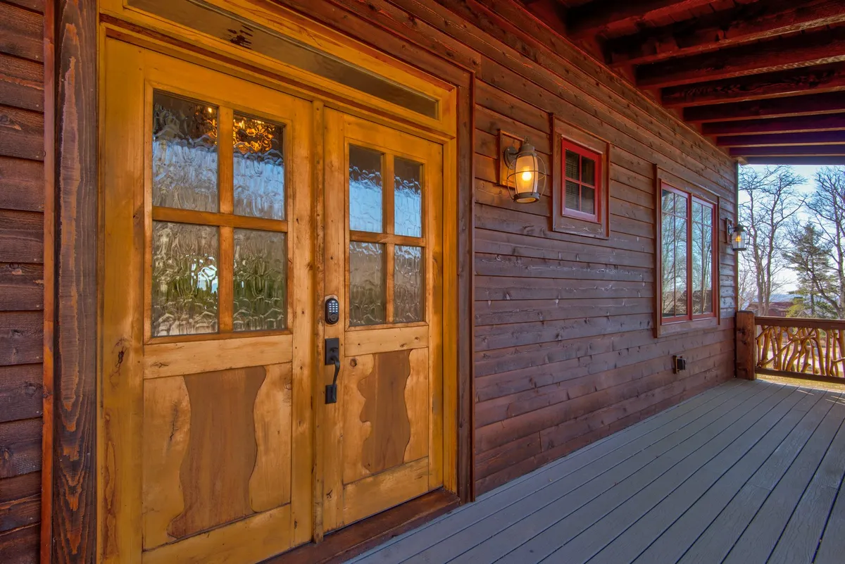 A close-up exterior view of an ornate wooden door with textured glass panels and rustic siding, highlighted by a decorative light fixture. The entryway creates a warm, inviting first impression and hints at gatherings within.